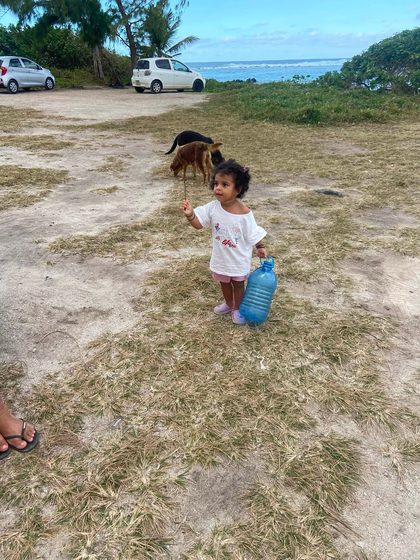 Toddler holding a water bottle near a dog on a grassy coastal parking area