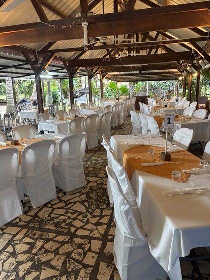The venue set up before guests arrived: tables in white with gold runners and white chair covers under a wooden roof, table number 1 in front
